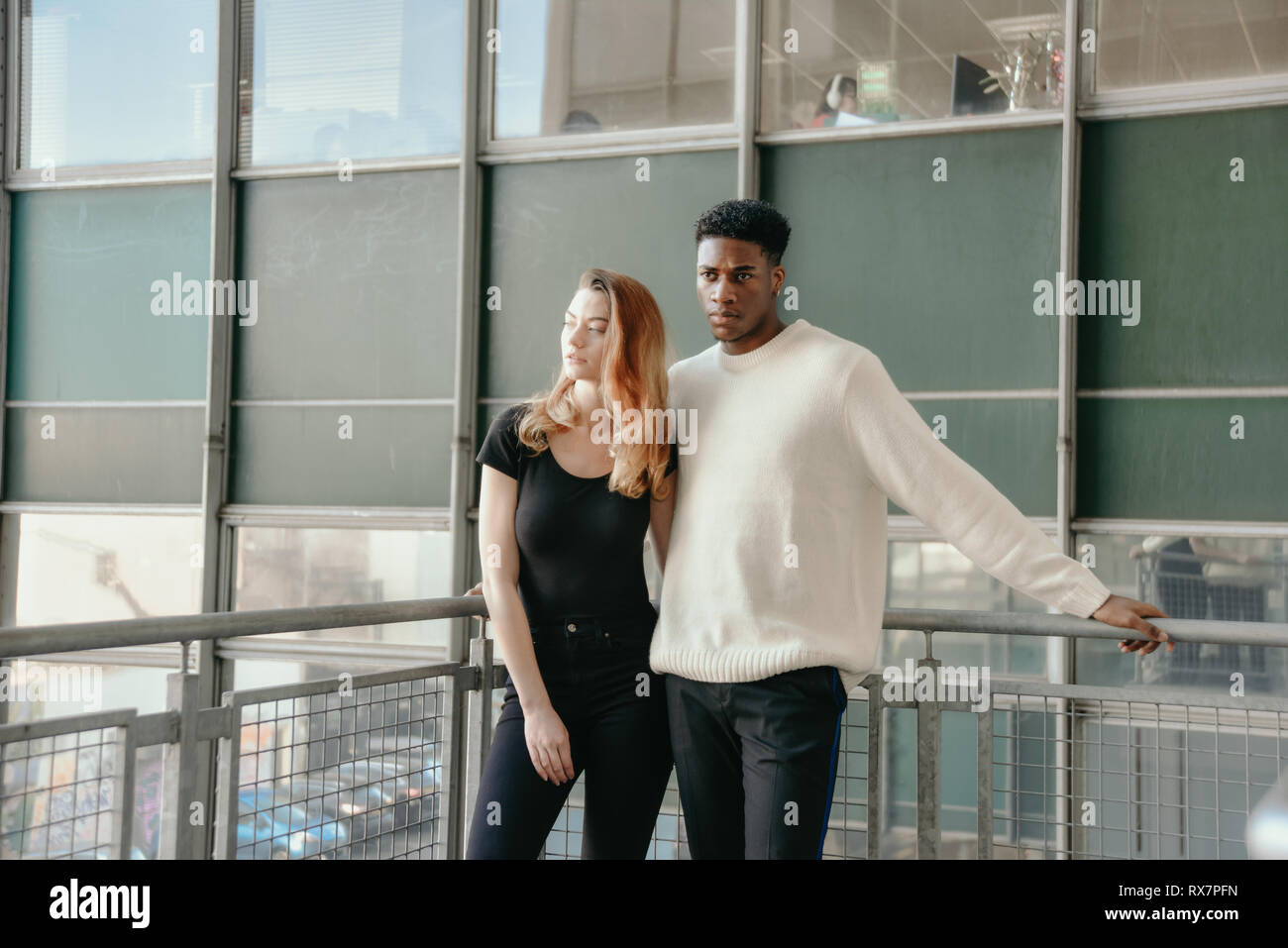 Ein gut aussehendes Paar stehen vor einem Modernistischen Tower Block in einer Stadt. Sie weiß ist er schwarz ist, sie sind ernst Stockfoto