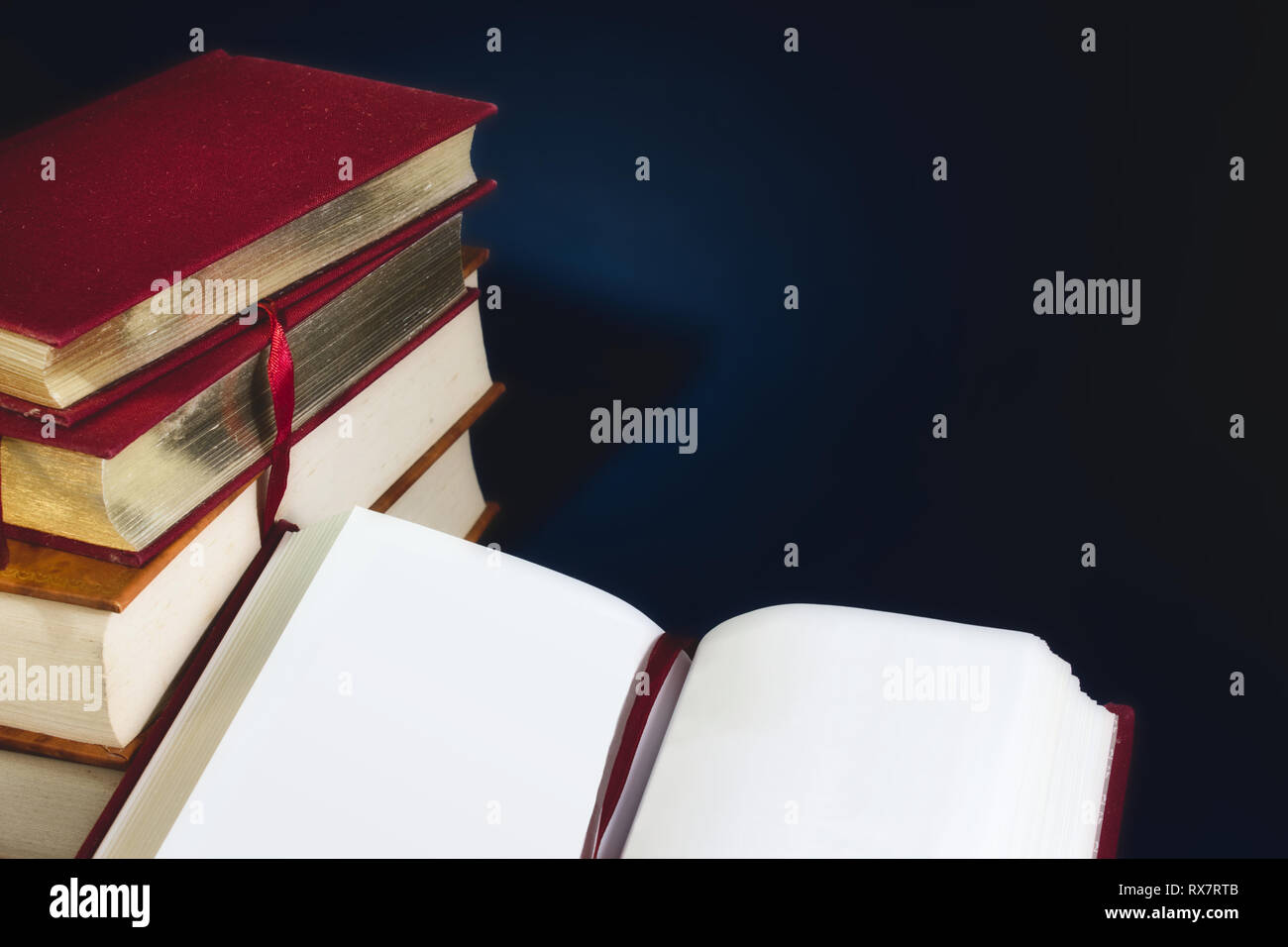 Stapel alter Bücher und ein offenes Buch mit Leeren leeren Seiten gegen einen dunkelblauen Hintergrund mit Speicherplatz für eigene Text kopieren Stockfoto