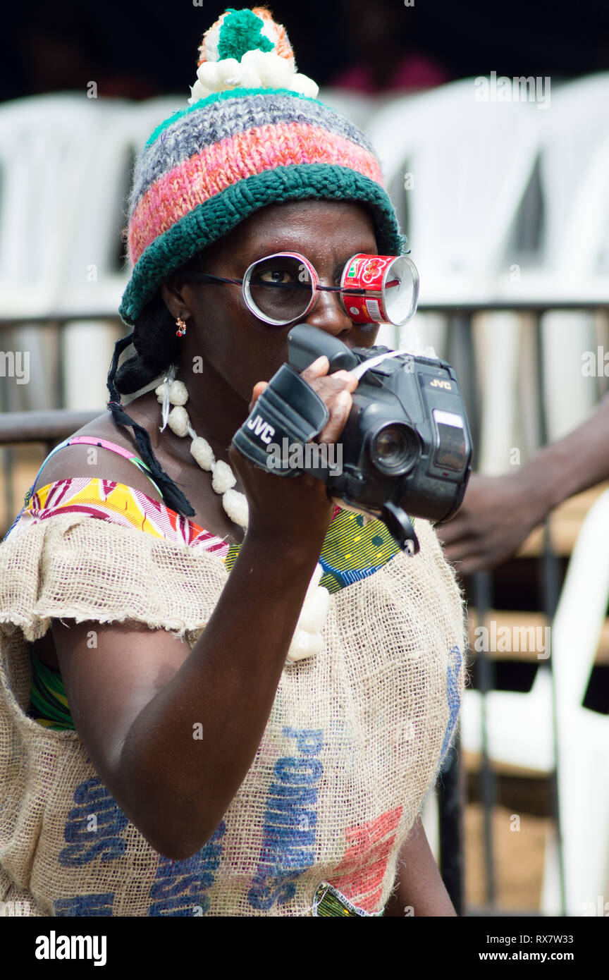 Bassam, Côte d'Ivoire - November 7, 2015: eine erwachsene Frau in einem Wolle hat, Vision Brille durch Boxen von Tomaten und tragen ein Unterhemd in Beuteln von coc Stockfoto