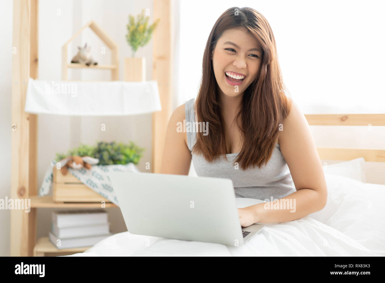 Glückliche junge asiatische Frau die Arbeit mit einem Laptop im Schlafzimmer Stockfoto