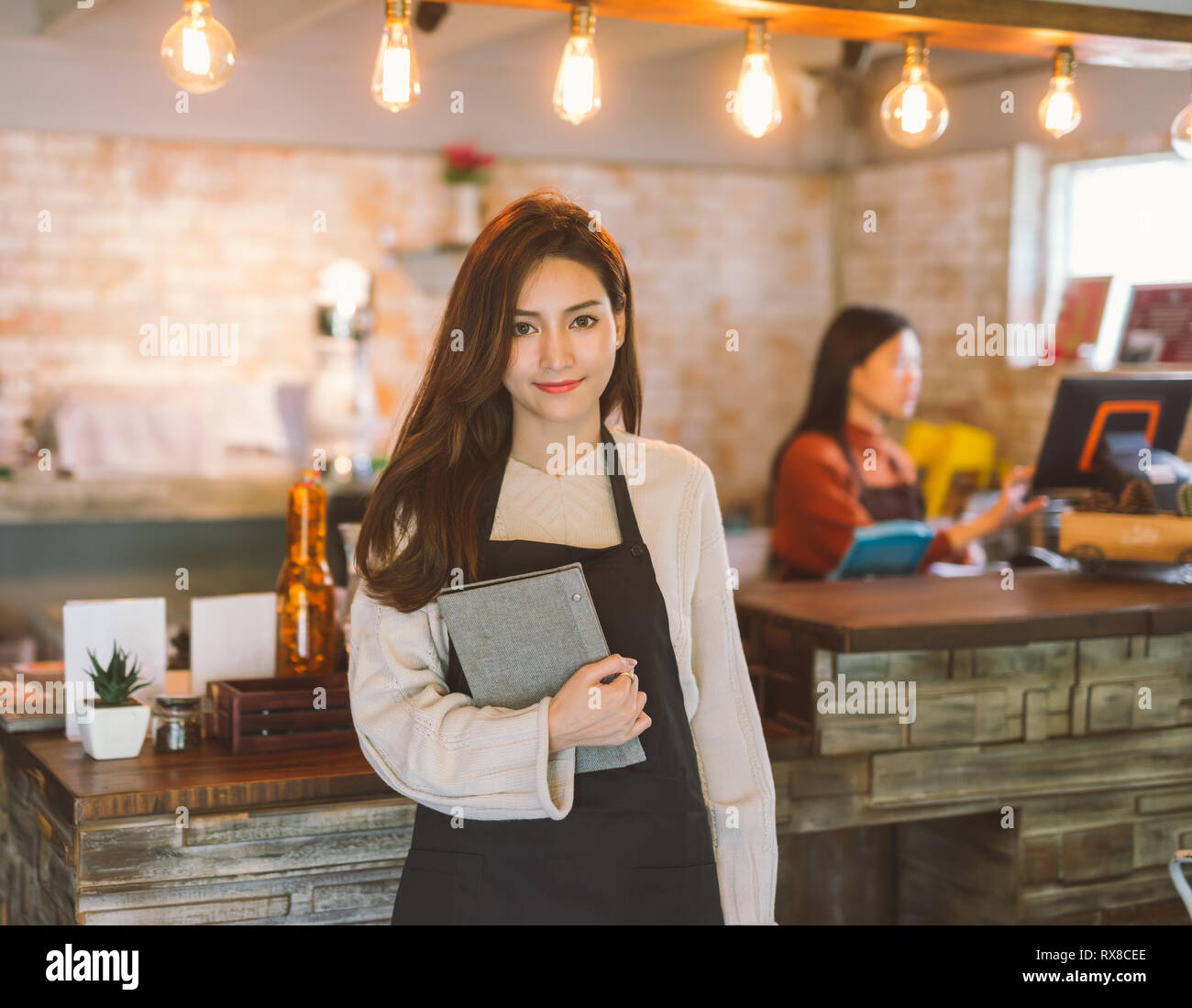 Portrait von asiatischen Mädchen Kellnerin holding Menü tragen Schürze und Stellung im Coffee Shop. Stockfoto