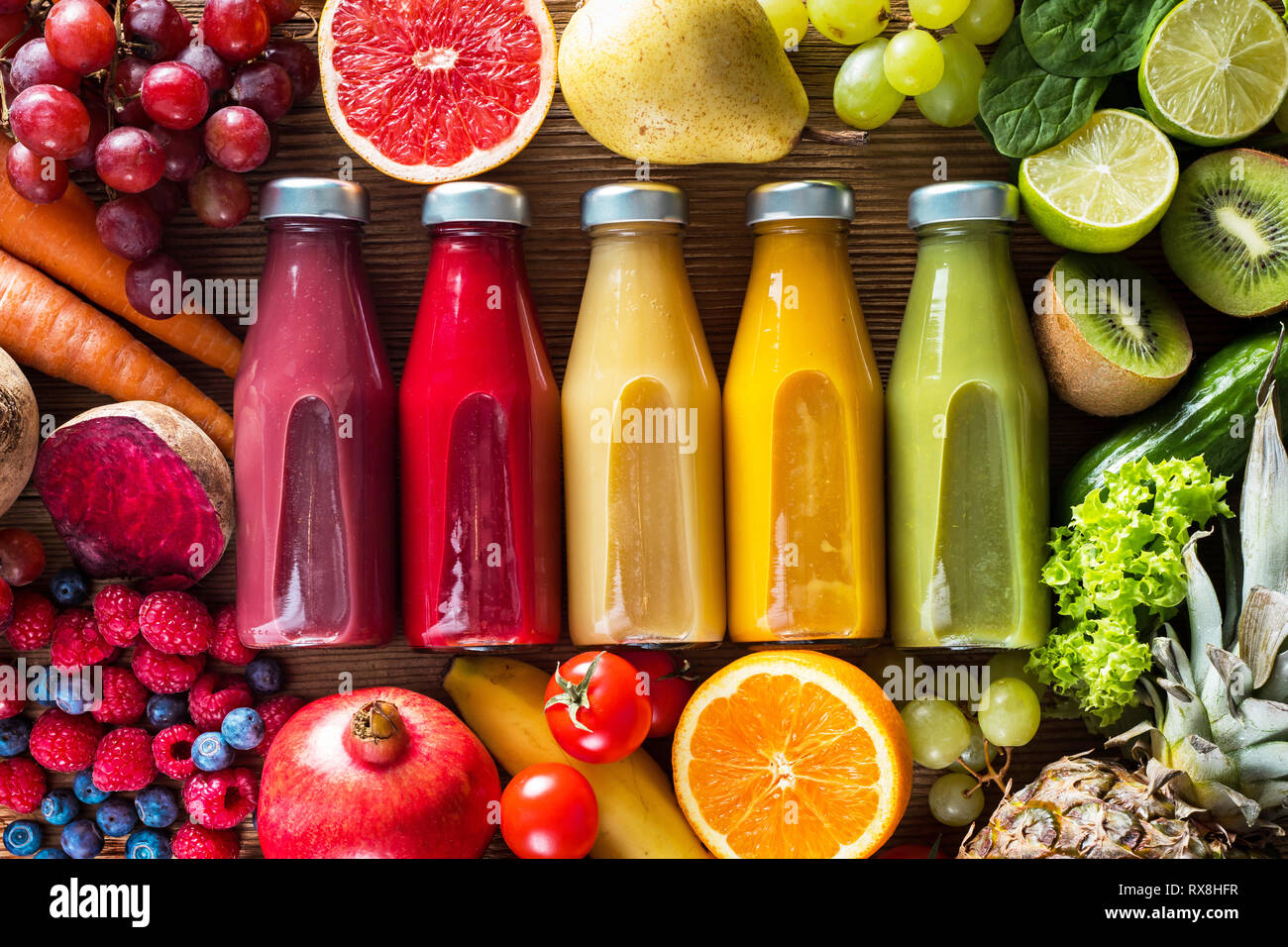 Bunte Smoothies in Flaschen und frische Obst und Gemüse auf Holztisch, Ansicht von oben. Stockfoto