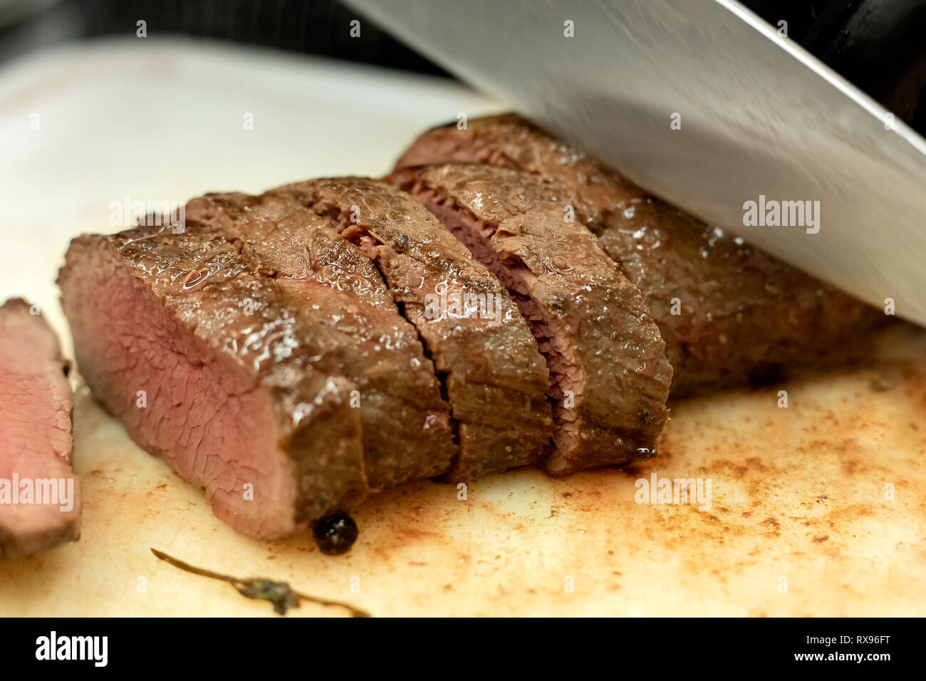 Carving, frisch zubereiteten sous vide Schweinefleisch auf weißem Kunststoff Schneidbrett mit einem grossen Messer. Stockfoto