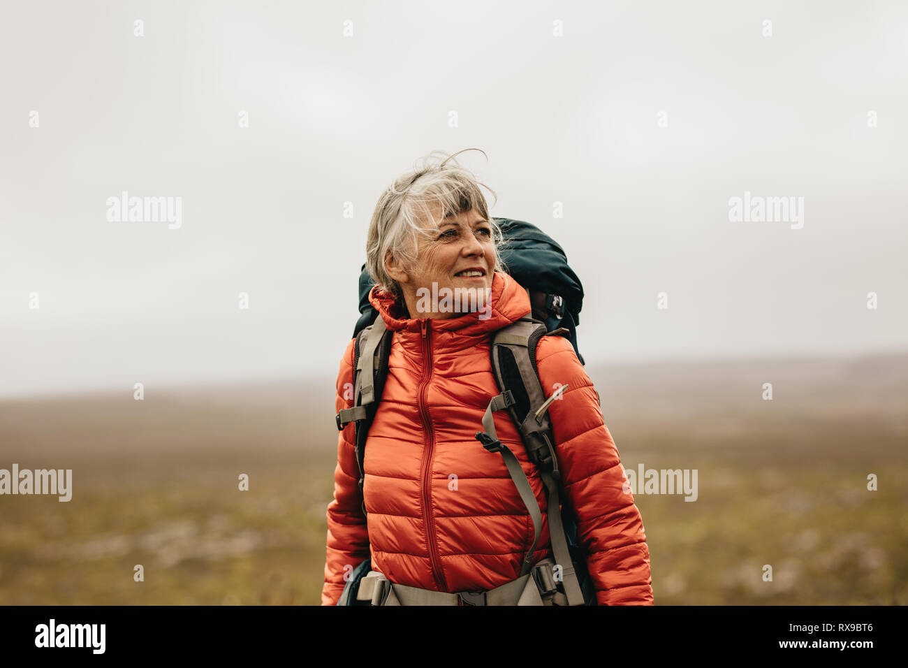 Ältere Frau, die auf einem Hügel trägt einen Rucksack und Wegsehen. Abenteuer sucht Frau trekking auf einem Hügel. Stockfoto