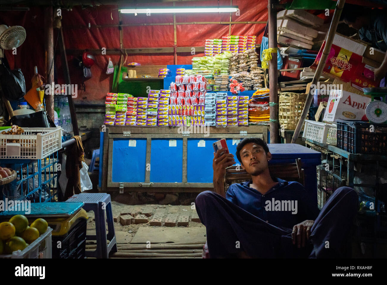 Mann vor seinem Laden in der Nähe der Autobahn Thiri Mandalar Busbahnhof, Mandalay, Myanmar sitzen. Stockfoto