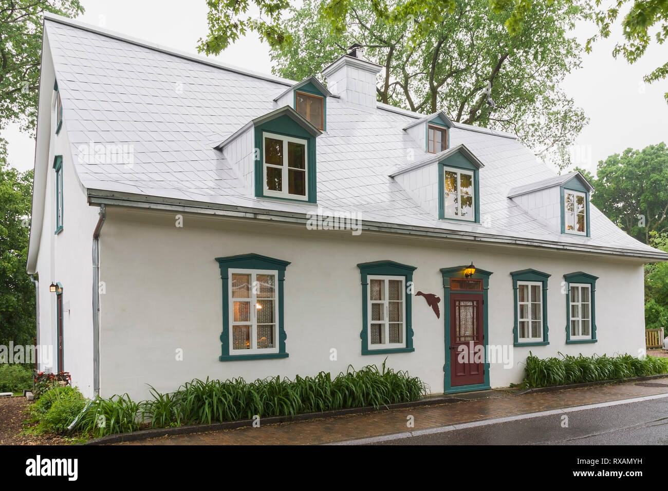 Beleuchtetes altes ca. 1805 weißes Raufußgemisch mit grünen und burgunderroten Zierleisten, Canadiana Cottage Stil Hausfassade im späten Frühjahr, Quebec, Kanada. Dieses Bild ist Eigentum freigegeben. CUPR0323 Stockfoto