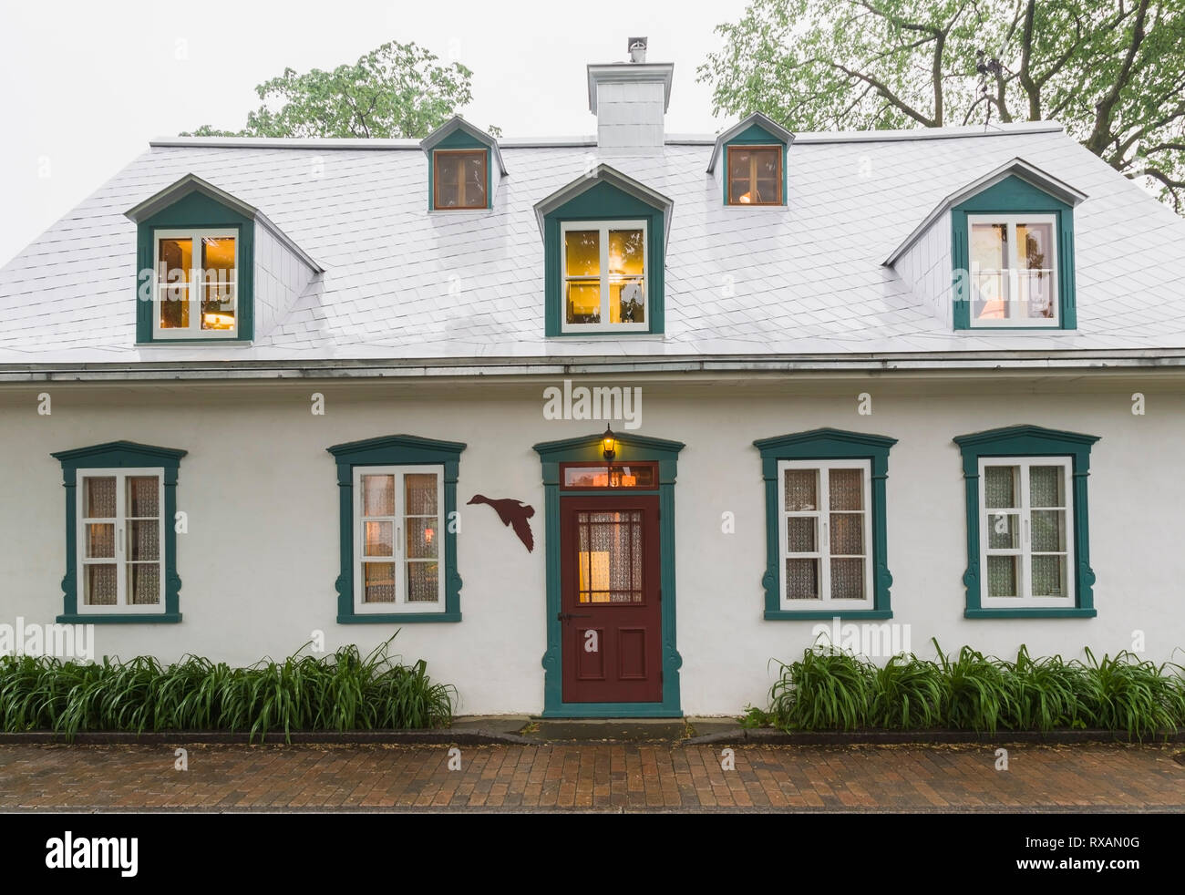 Beleuchtetes altes ca. 1805 weißes Raufußgemisch mit grünen und burgunderroten Zierleisten, Canadiana Cottage Stil Hausfassade im späten Frühjahr, Quebec, Kanada. Dieses Bild ist Eigentum freigegeben. CUPR0323 Stockfoto