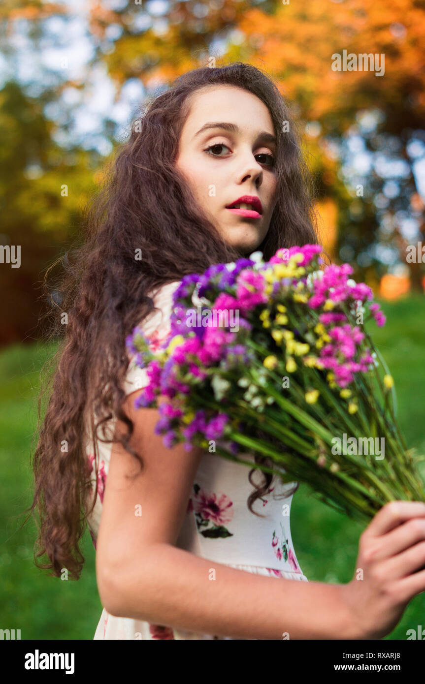 Low Angle Portrait von Frau mit bunten Blumen, während sich gegen Bäume im Park im Herbst Stockfoto