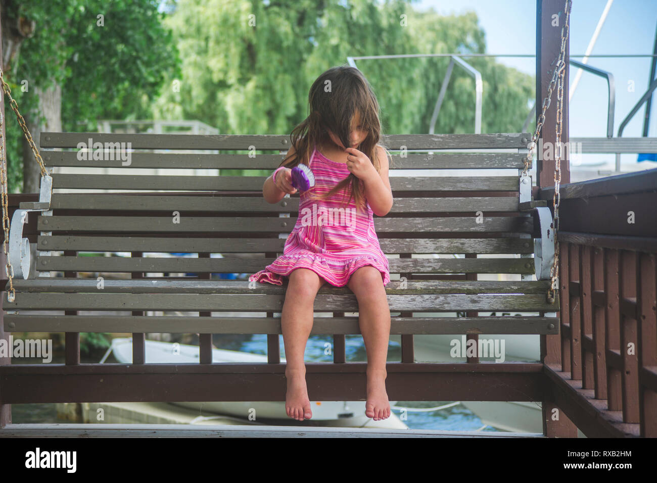 Mädchen bürsten Haar, während auf hölzernen Schwingen in der Veranda sitzen Stockfoto