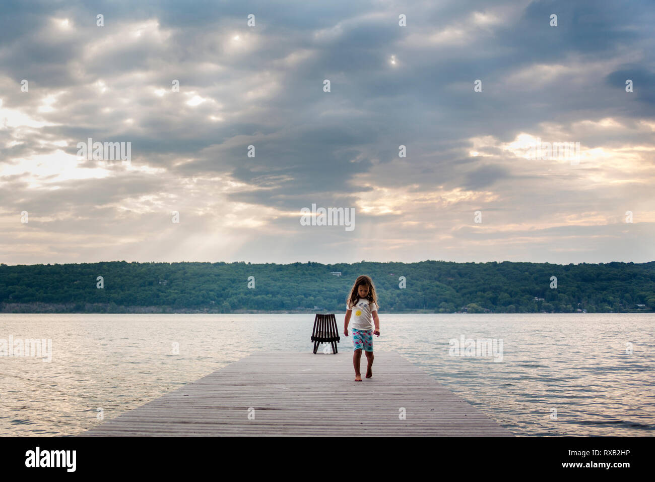 Mädchen gehen auf Pier über den See gegen bewölkter Himmel bei Sonnenaufgang Stockfoto