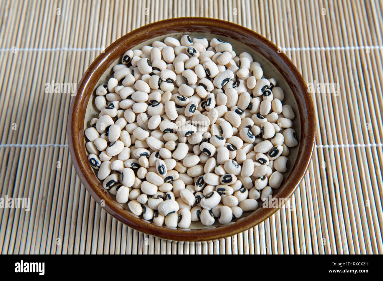 Black Eyed Beans in Vintage braun Keramik Topf auf Tischset. Stockfoto