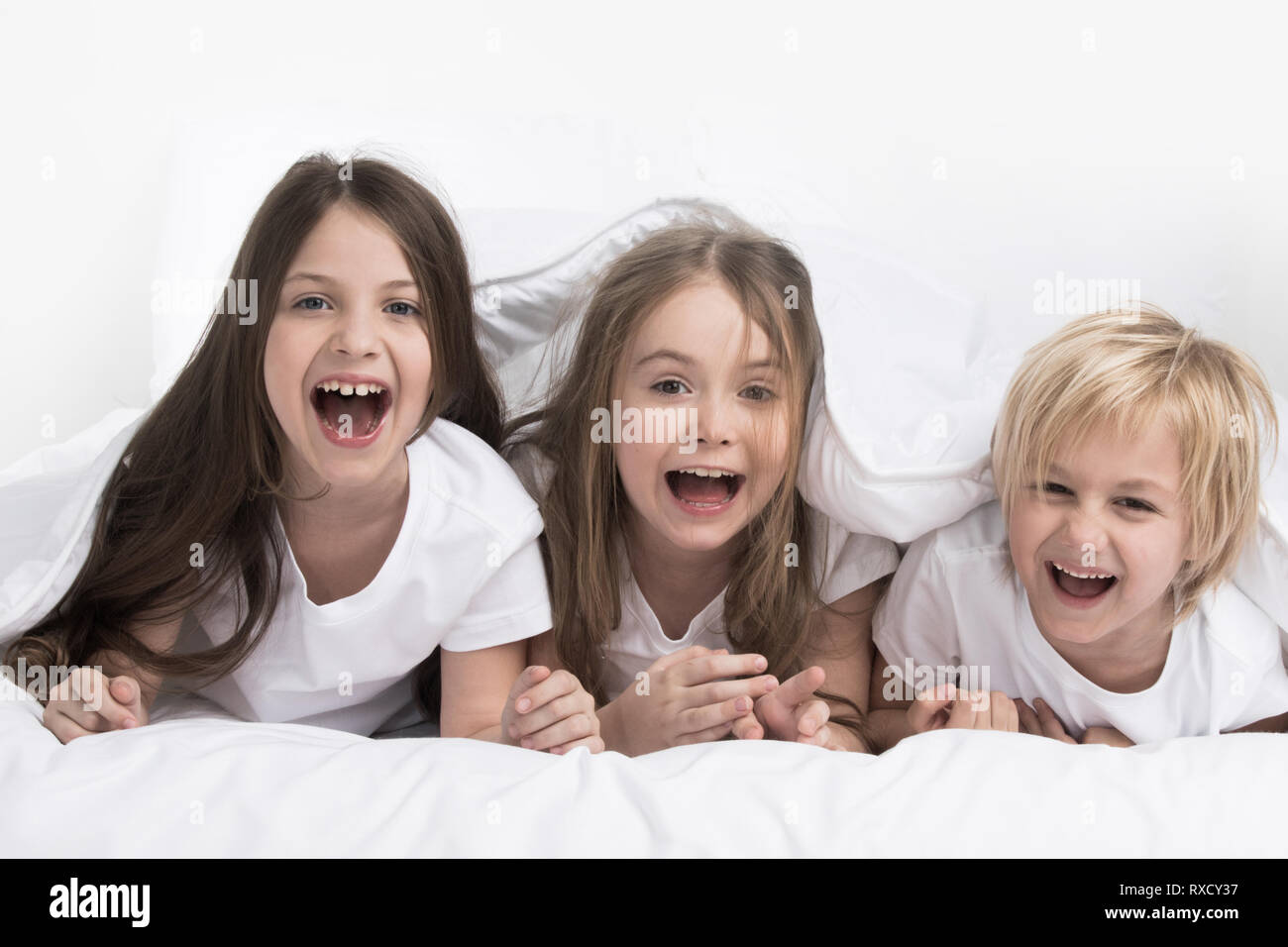 Gerne drei Kinder unter einer Decke auf weißem Hintergrund Stockfoto