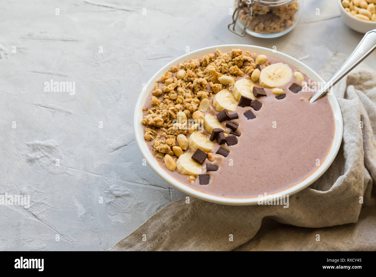 Schokolade smoothie Schüssel mit Bananen, Müsli und Erdnüsse auf Hellgrau konkreten Hintergrund. Gesundes vegetarisches Frühstück. Stockfoto