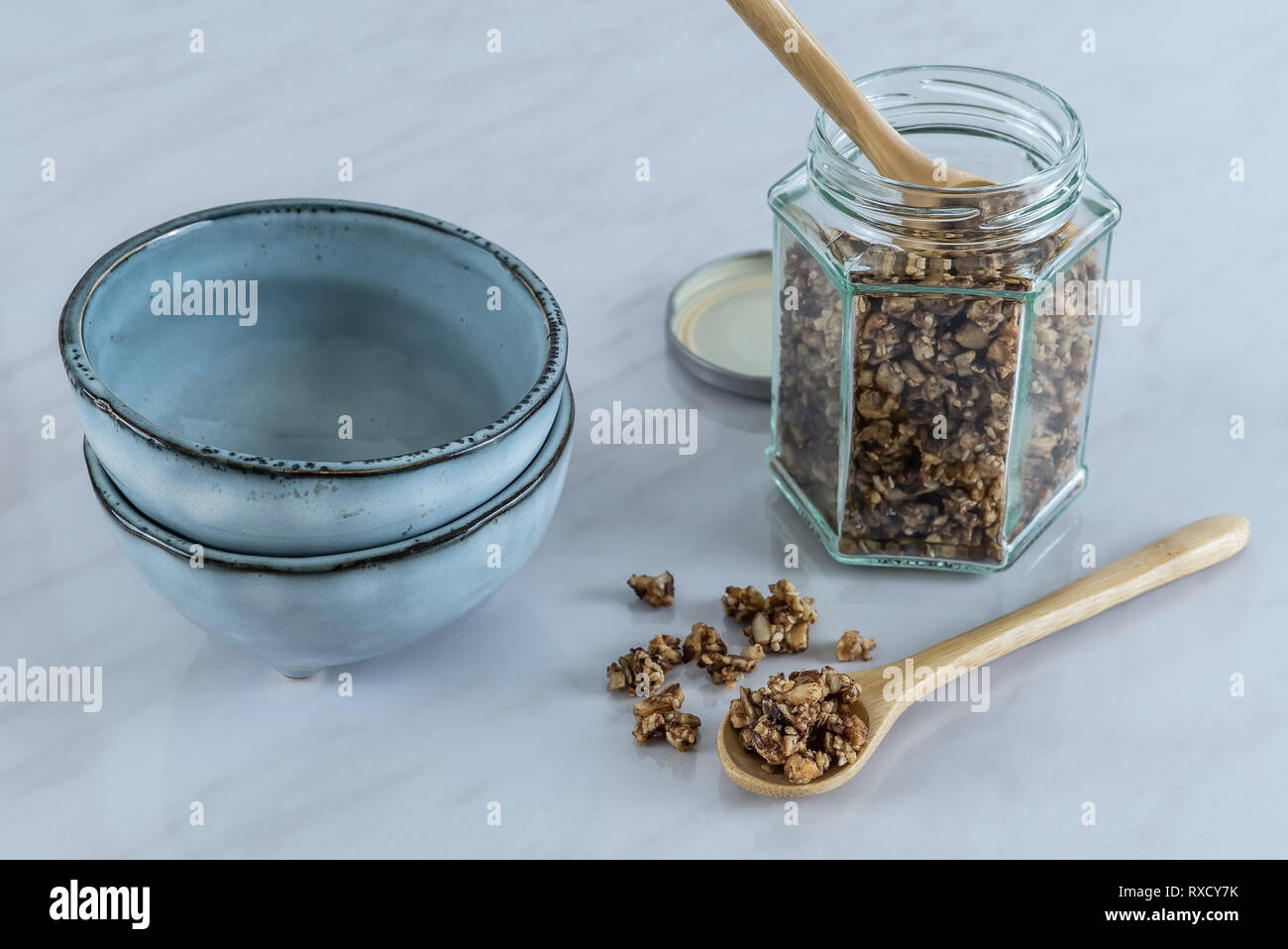 Hausgemachten gesunden und nahrhaften Frühstück Müsli in einem Glas mit Holz, Löffel und blau Keramik Schalen auf Marmor Küchentisch in frischen Morgen Licht Stockfoto