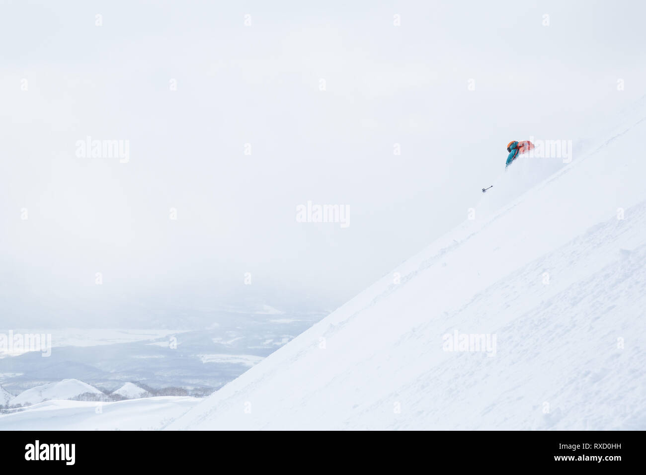 Backcountry Skiing hinter Niseko, Moiwa in Hokkaido, Japan. Skifahrerin Sprays, Puder, als sie dreht sich auf einem Hang über ein breites Tal an einem bewölkten d Stockfoto