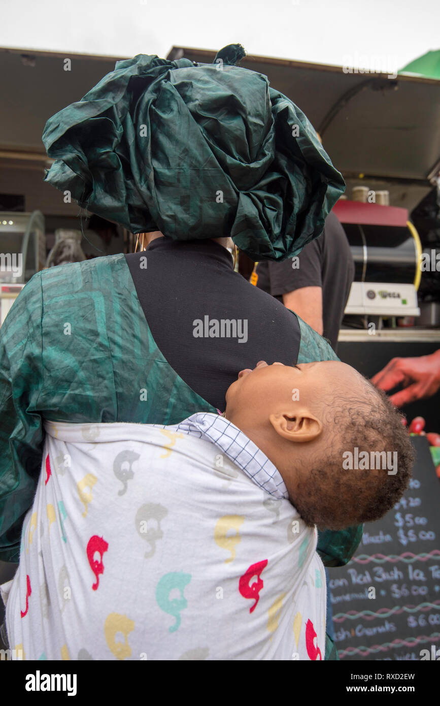 9 Mar 2019, eine Frau in der Linie Kaffee mit ihrem schlafenden Baby auf dem Rücken kaufen am Africultures Festival Wyatt Park, Lidcombe, Sydney Australien. Stockfoto