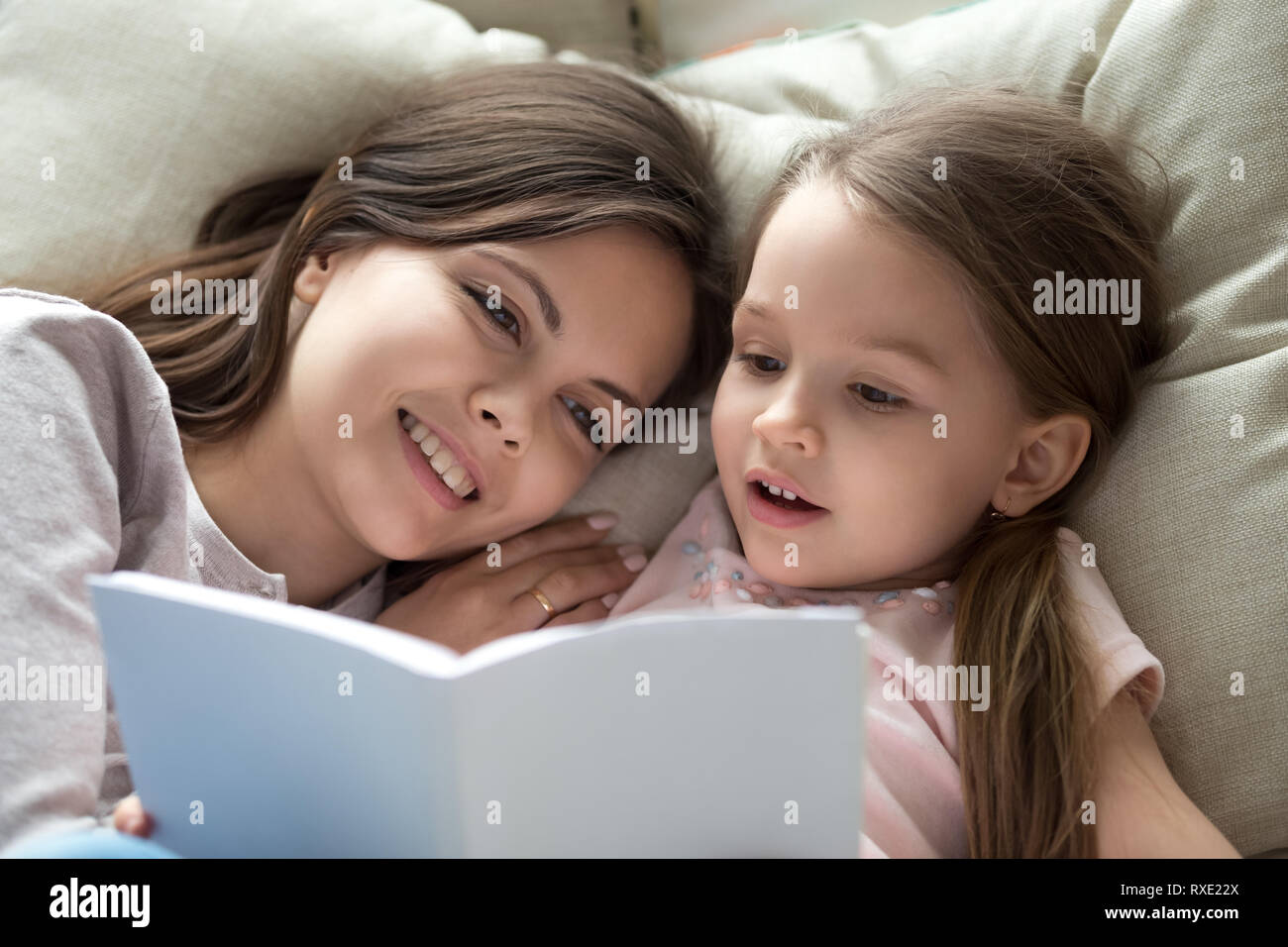 Glückliche Mutter hören Kind Tochter lernen Buch lesen im Bett Stockfoto
