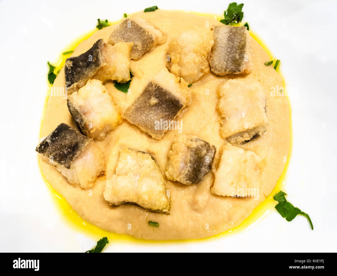 Italienische Küche - Blick von oben auf die Stücke von Baccala (Stockfisch) mit pürierten Kichererbsen schließen bis auf weiße Platte in einem lokalen Restaurant in der Lombardei Stockfoto