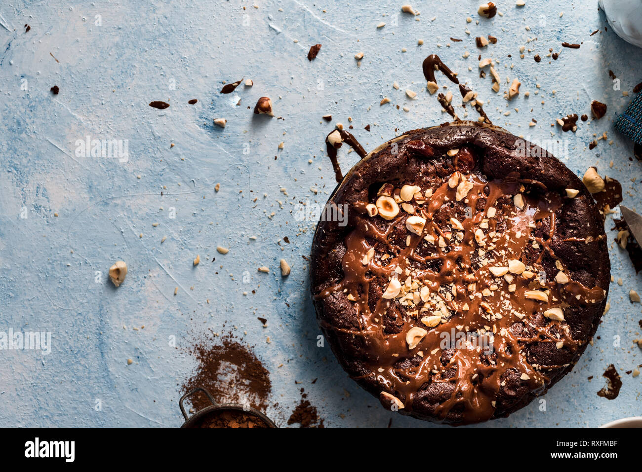 Schokoladenkuchen auf einem blauen strukturierten Hintergrund mit etwas verschüttet, Schokolade und gehackte Haselnüsse Stockfoto