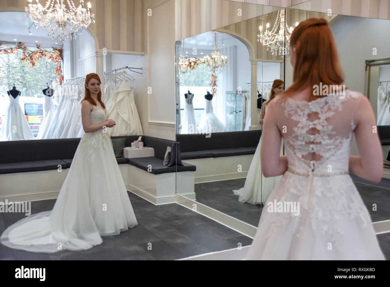 Eine hübsche rothaarige Mädchen ist in einer Wedding Dress Shop suchen t und versuchen, auf weiße Brautkleider Stockfoto