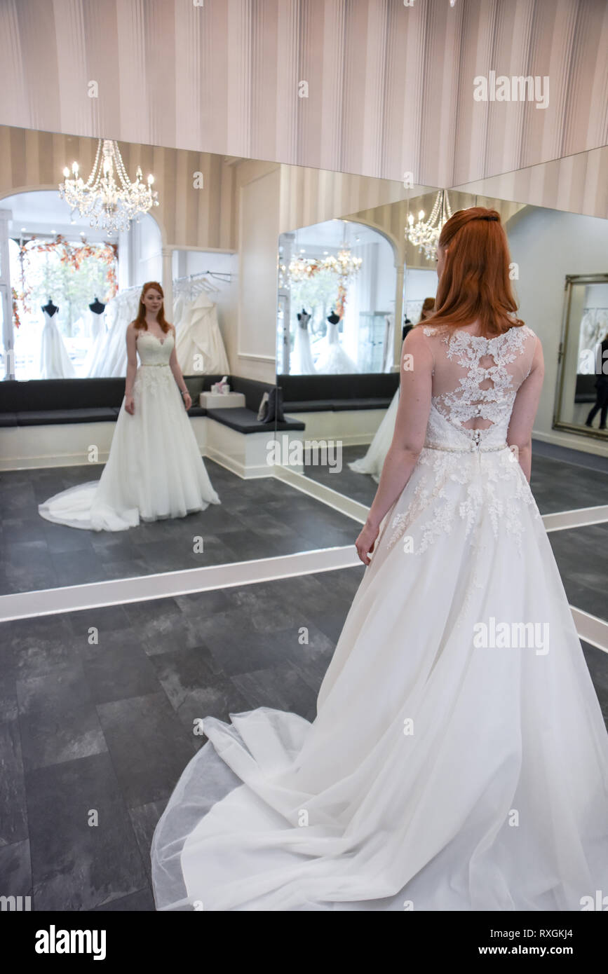 Eine hübsche rothaarige Mädchen ist in einer Wedding Dress Shop suchen t und versuchen, auf weiße Brautkleider Stockfoto