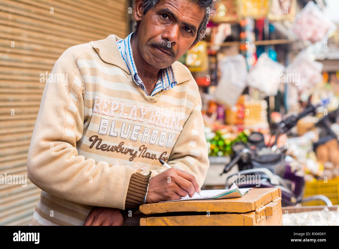 Ein indischer Mann mittleren Alters tragen Pullover stehend, in die Kamera schaut und hat ein Notebook öffnen am Nachmittag im Winter. Er ist 50-55 Jahre alt. Stockfoto