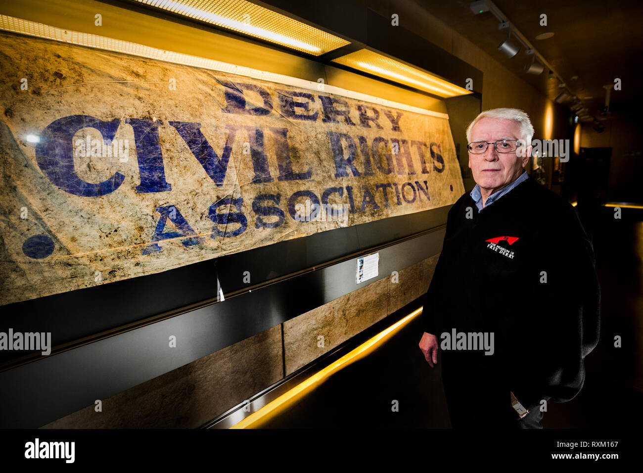 John Kelly, deren 17 Jahre alten Bruder, Michael, während der blutige Sonntag getötet wurde, steht neben der Derry Civil Rights Association Banner im Museum von Free Derry, dass an dem Tag, als blutiger Sonntag bekannt ist, durchgeführt wurde. Die Staatsanwaltschaft wird erwartet, zu verkünden, ob es Ermittlungen gegen Soldaten über den Tod von 13 Menschen in Londonderry am 30. Januar 1972 fortzusetzen. Stockfoto