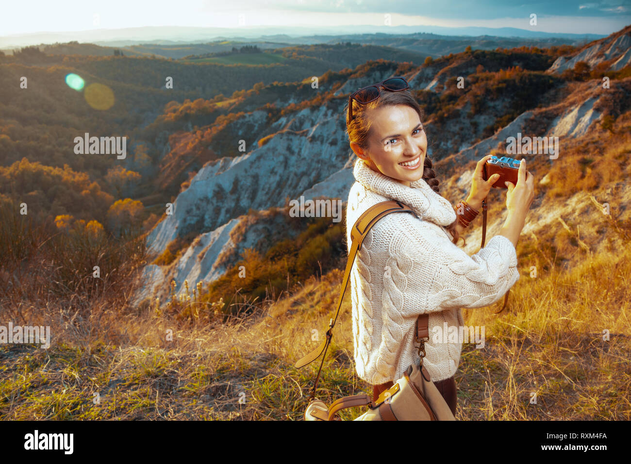 Lächelnden jungen touristische Frau in Wanderausrüstung mit Tasche die Bilder mit retro Foto Kamera gegen Sommer Landschaft der Toskana, Italien. Stockfoto