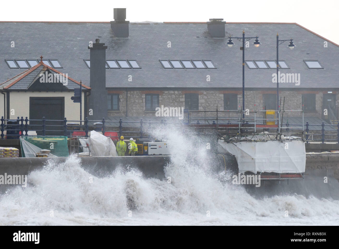 Wellen gegen die hafenmauer als Arbeitnehmer arbeiten am Meer Verteidigung während eines Sturms auf Porthcawl, Wales durchführen. Das Met Office haben einen gelben w ausgestellt Stockfoto