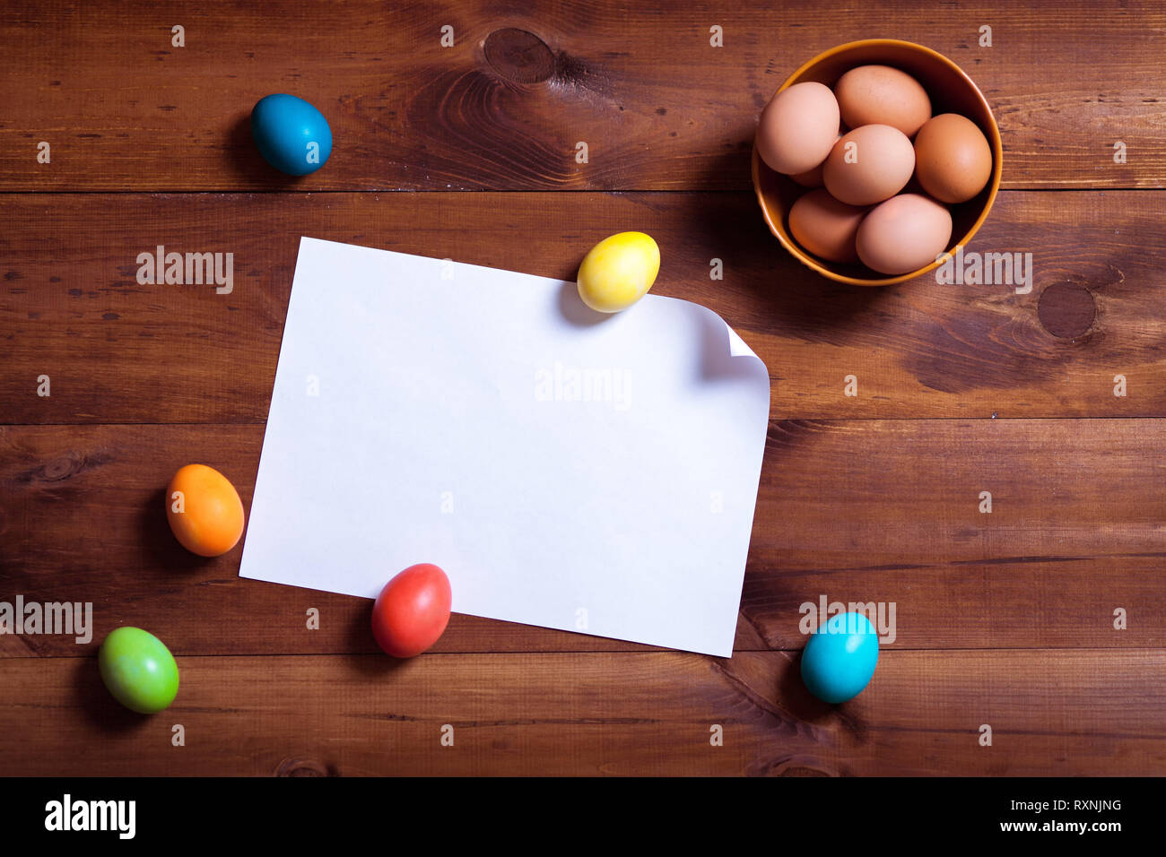 Frohe Ostern Hintergrund, bunte Eier und leeres weißes Papier auf braune Holztisch, Frühling Spaß dekoration design, traditionelle April celebrat Stockfoto