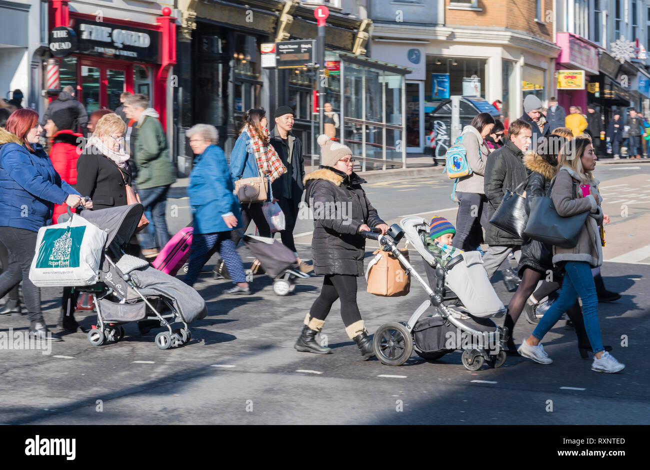 Menschen schieben Kinderwagen mit Kindern über eine belebte Straße in Brighton, East Sussex, England, Großbritannien. Menschen, die vielbefahrene Straßen überqueren. Jeden Tag. Stockfoto