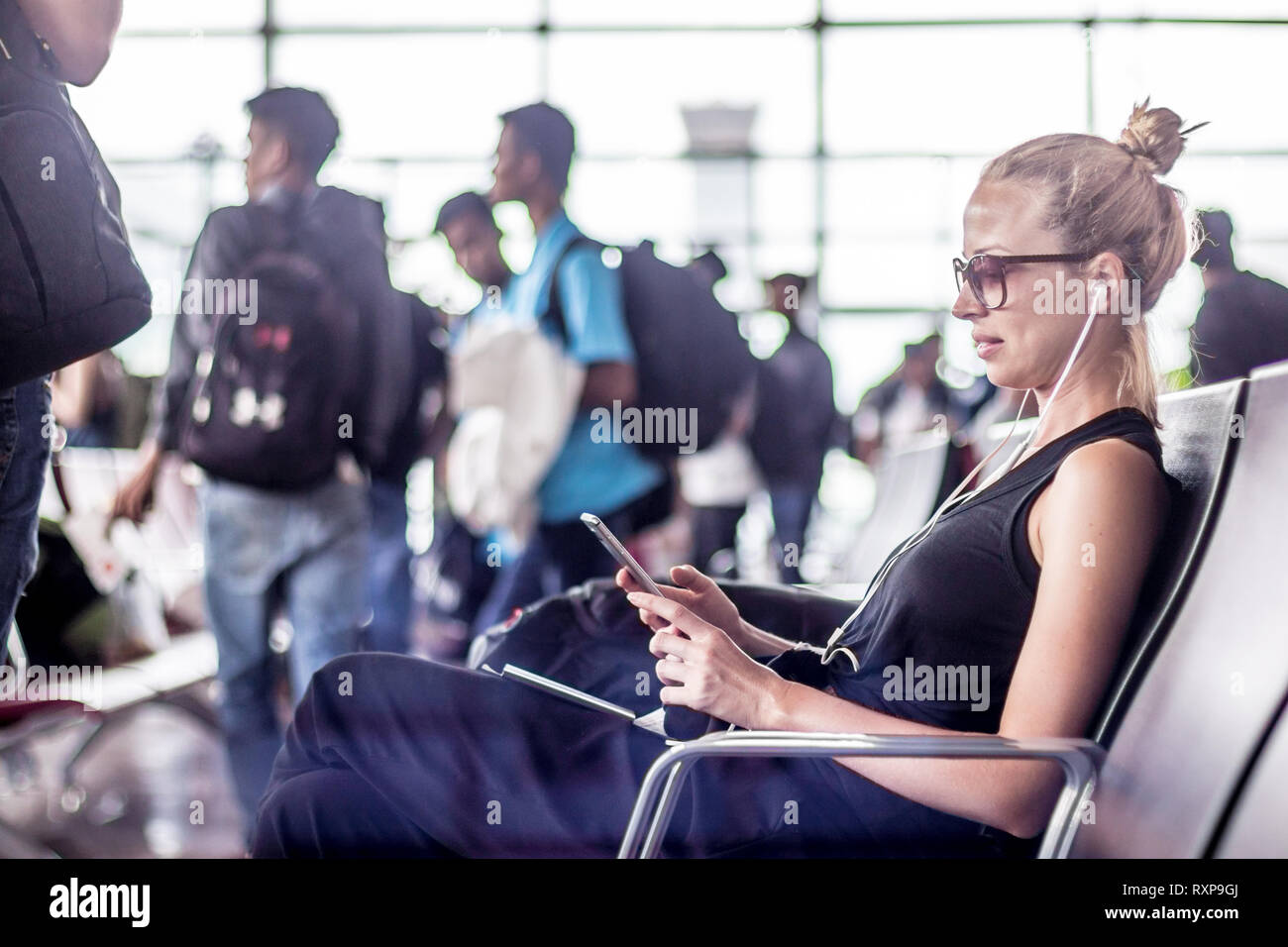 Weibliche Reisende können Sie über Ihr Handy während der Wartezeit in ein Flugzeug steigen bei der Abreise Gates in asiatischen Flughafen Terminal. Stockfoto