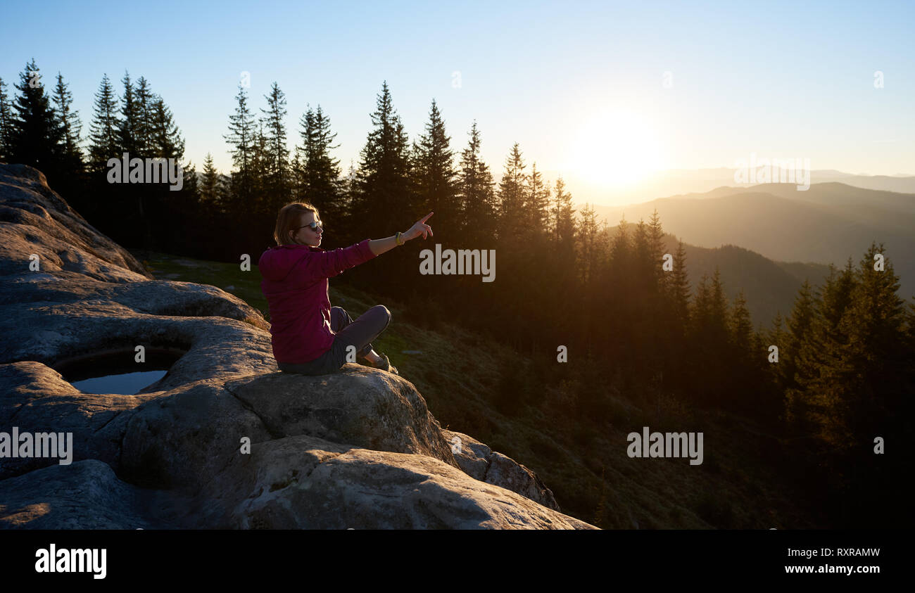 Junge Frau Touristen sitzen auf großen Felsen auf dem Gipfel des Berges in den Morgen. Aktive weibliche Touristen in unglaublich schönen Sonnenaufgang zeigt. Am b Stockfoto