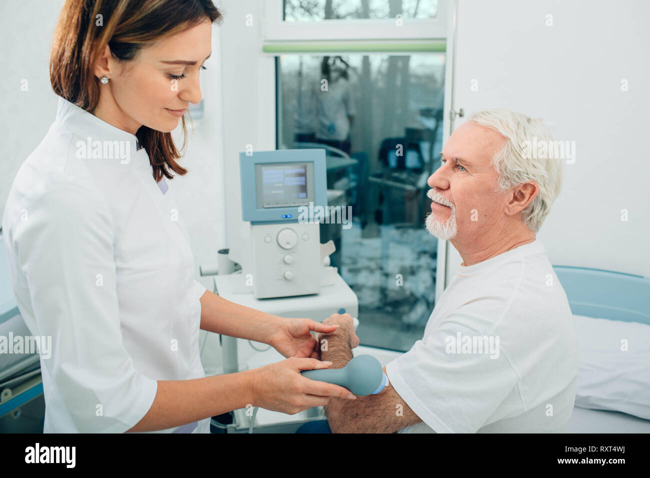 Physiotherapeut mit Ultraschall Maschine an Hand von Client in der Klinik. Physiotherapeutische Behandlung Stockfoto
