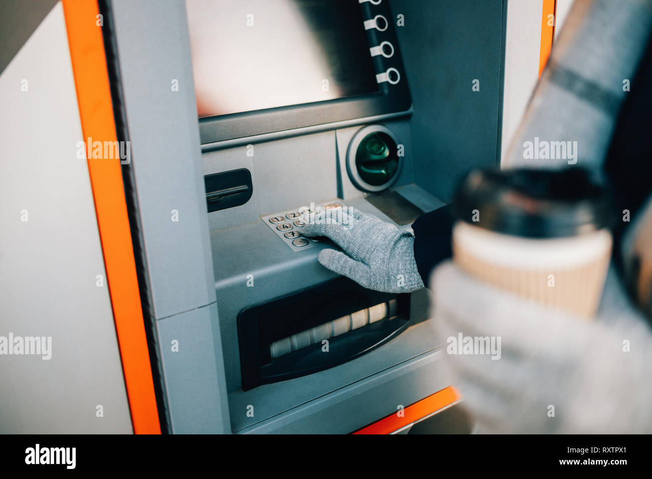 Nicht erkennbare junge Frau Tasten auf ATM-Tastatur Eingabe von PIN und Kaffee trinken auf der Straße im Winter Tag, close-up. Stockfoto