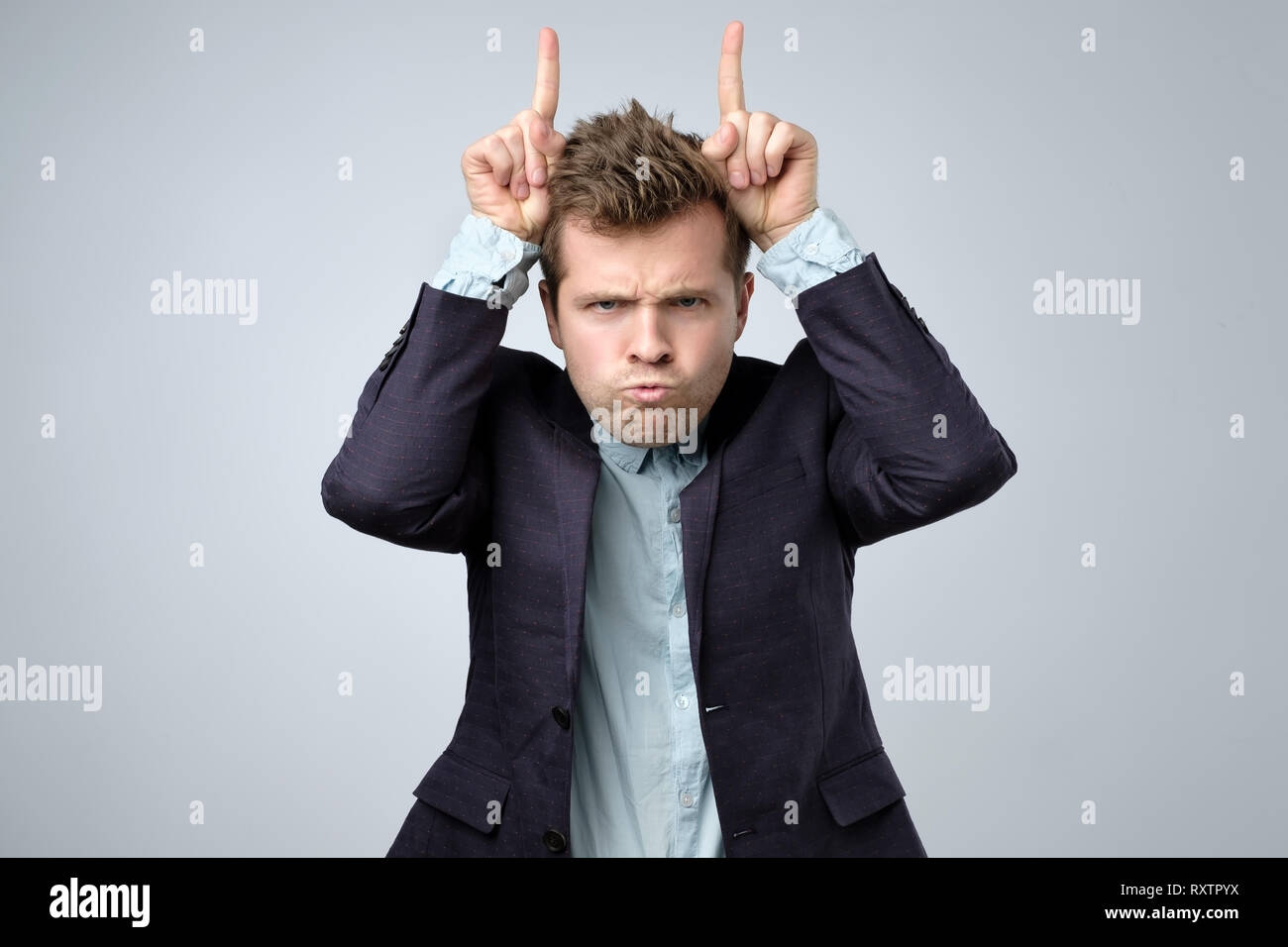 Verspielt aussehenden bärtigen Mann in Anzug an Kamera mit lustigen Gesicht und Hörner Finger suchen Stockfoto