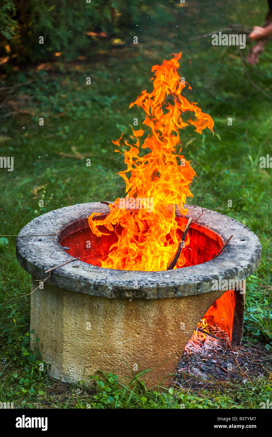 Trockene Zweige brennen in isolierten Lagerfeuerplatz im Garten. Hohe helle Flammen Flackern auf offenen Garten Feuerstelle. Vertikale Foto Stockfoto