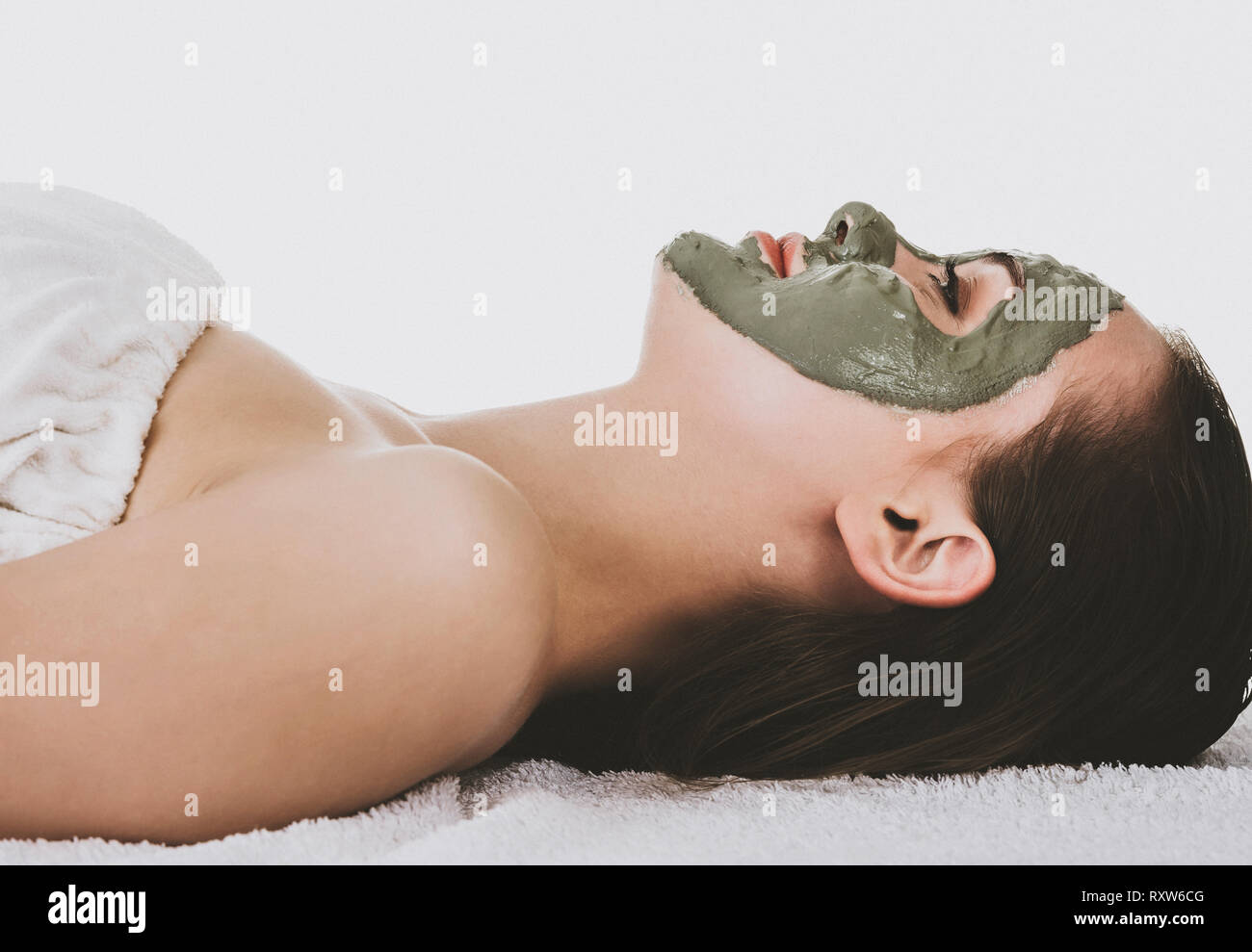 Seitenansicht der liegenden Frau mit grünen Gesichts Clay Mask, weisser Hintergrund. Stockfoto