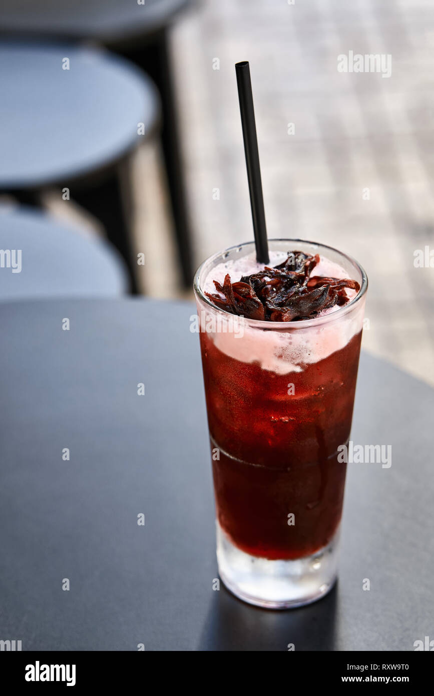 Red Cocktail mit einem schwarzen Stroh auf die dunkle runde Tisch im Café draußen auf den verschwommenen Hintergrund. Closeup vertikale Foto. Stockfoto