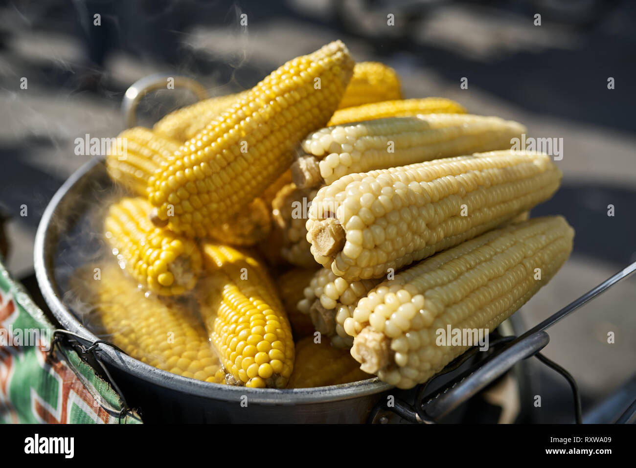 Heiß gekocht gelber Mais in der Metall Kochtopf auf den Markt auf der sonnigen Hintergrund im Freien. Dampf steigt über Sie. Closeup horizontale Foto. Stockfoto