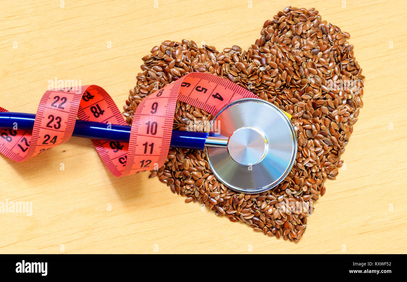 Ernährung Gesundheit Gewichtsreduktion Konzept. Leinsamen Leinsamen herzförmige Stethoskop und Maßband. Gesunde Ernährung zur Vorbeugung von Herzkrankheiten, Stockfoto