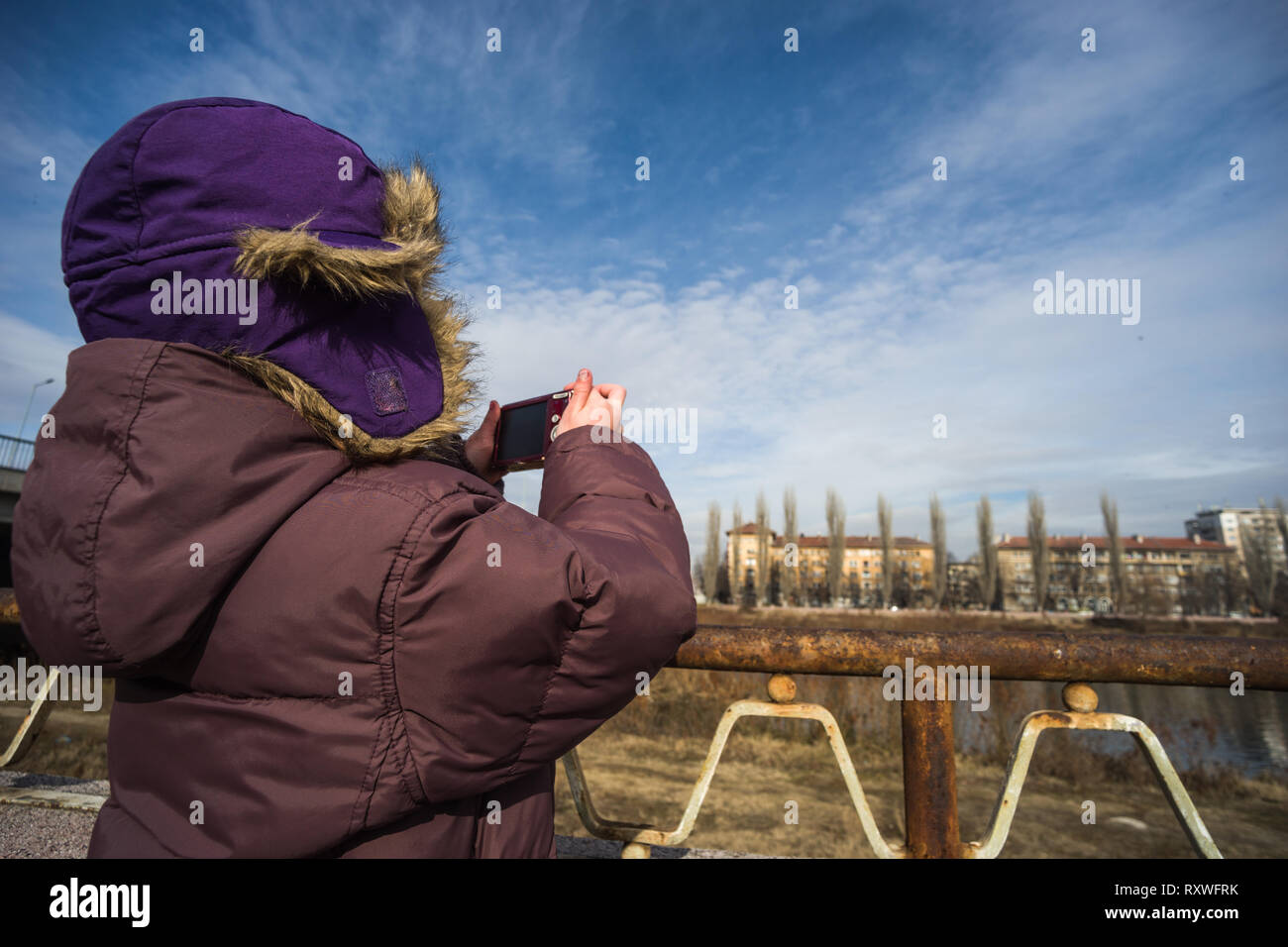 Kind mit lila Winterjacke und einen Hut mit einer Kamera auf einem blauen Himmel Hintergrund Stockfoto