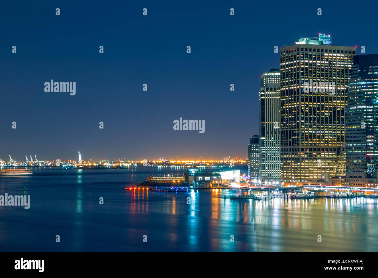USA. New York City. Nachtlichter von Manhattan Waterfront und die Freiheitsstatue am Horizont. Stockfoto