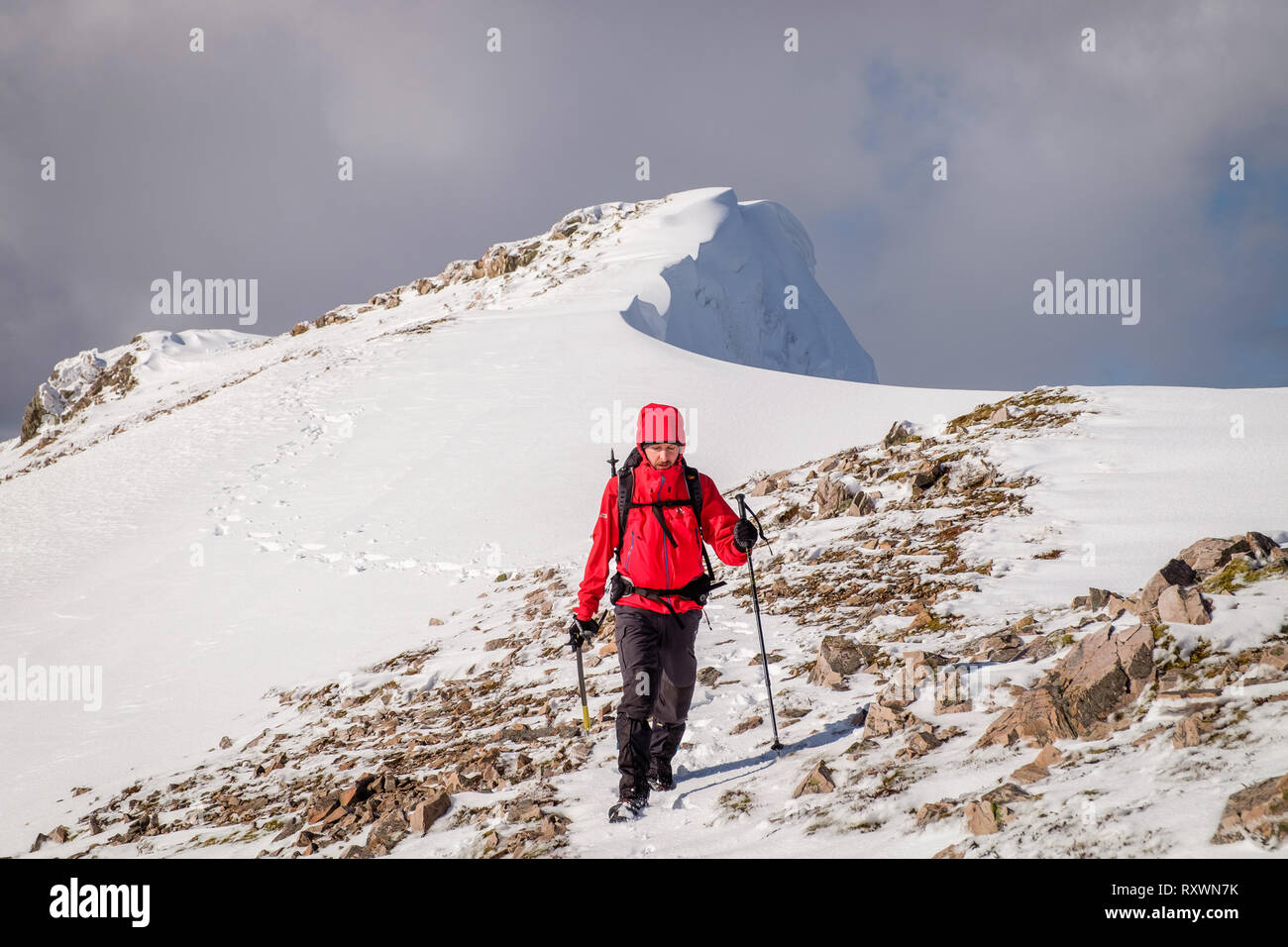 Mann im roten Mantel, mit Eispickel Wandern/Klettern im Winter auf Schnee bedeckten Berg in Schottland. Model Release - garbh Bheinn, Loch Leven Highlands Stockfoto