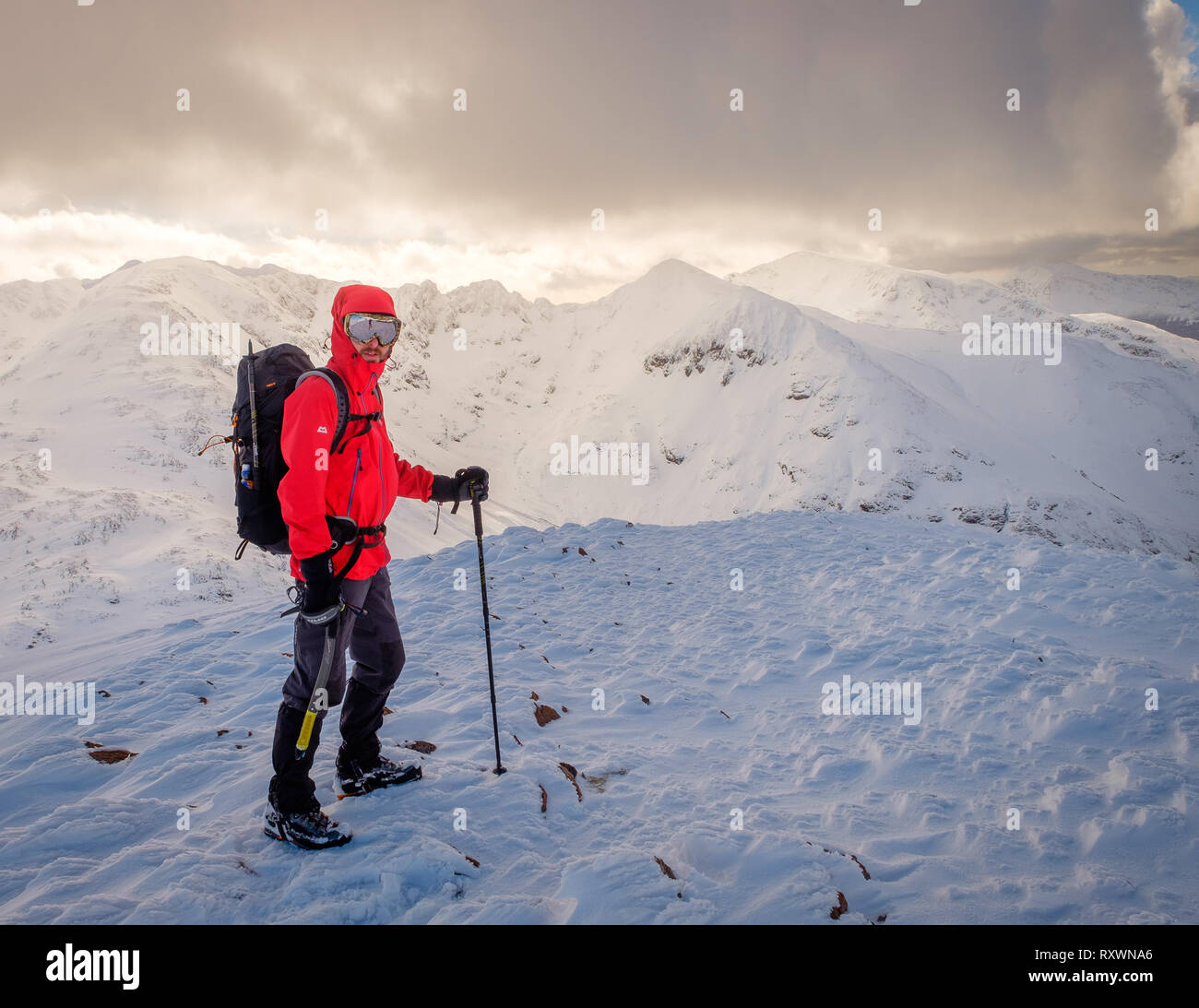 Mann im roten Mantel, mit Eispickel Wandern/Klettern im Winter auf Schnee bedeckten Berg in Schottland. Model Release - garbh Bheinn, Loch Leven Highlands Stockfoto