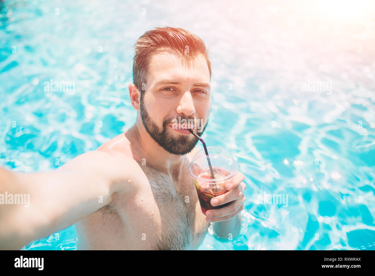 Happy bärtigen Mann, der selfie im Pool. Er trinkt einen Cocktail und entspannend. Stockfoto