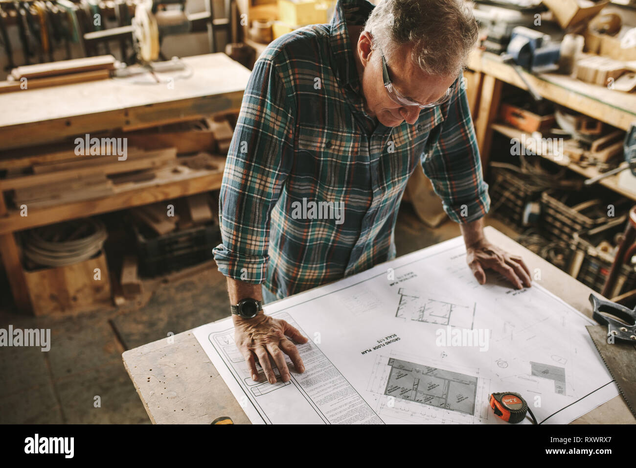 Senior Zimmermann Studium Blaupause in seiner Werkstatt vor Beginn seiner Arbeit. Tischler Kontrolle Zeichnung in der Schreinerei. Stockfoto