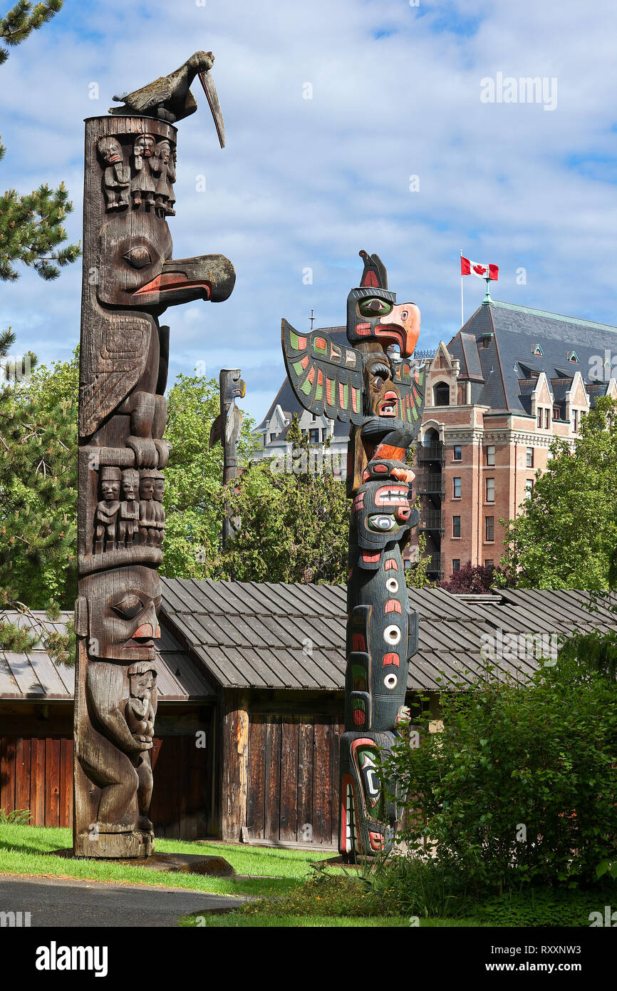 Gruppe von Totems an Thunderbird Park, Royal BC Museum, Victoria, British Columbia, Kanada. Im Hintergrund ist ein Teil der Fairmont Empress Hotel. Stockfoto
