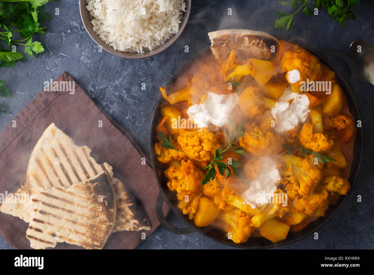 Vegetarisches indisches Essen. Blumenkohl curry Pfanne mit Basmati Reis und Naan Brot auf dunklem Stein Hintergrund der Ansicht von oben. Gesundes und schmackhaftes Essen Konzept Stockfoto