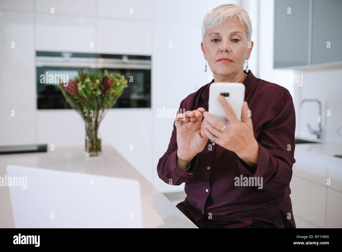 Porträt einer schönen reife Frau, mit Ihrem Mobiltelefon, in der Küche mit Laptop Stockfoto